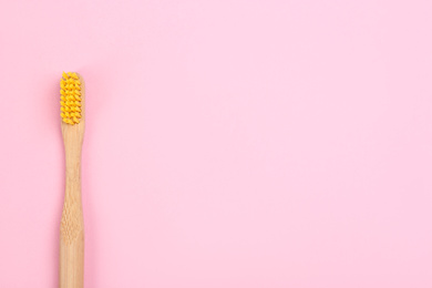 Toothbrush made of bamboo on pink background, top view. Space for text