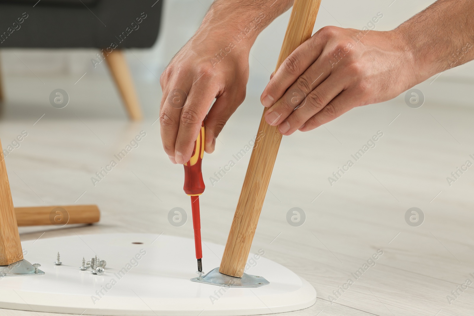 Photo of Man with screwdriver assembling furniture on floor indoors, closeup