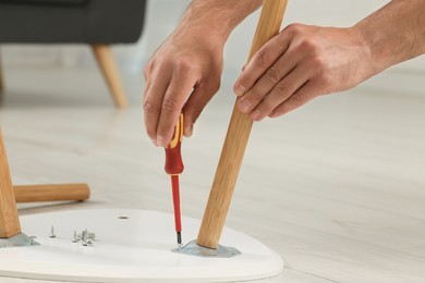 Photo of Man with screwdriver assembling furniture on floor indoors, closeup