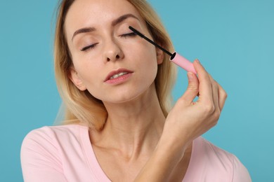 Photo of Woman applying mascara on light blue background, closeup