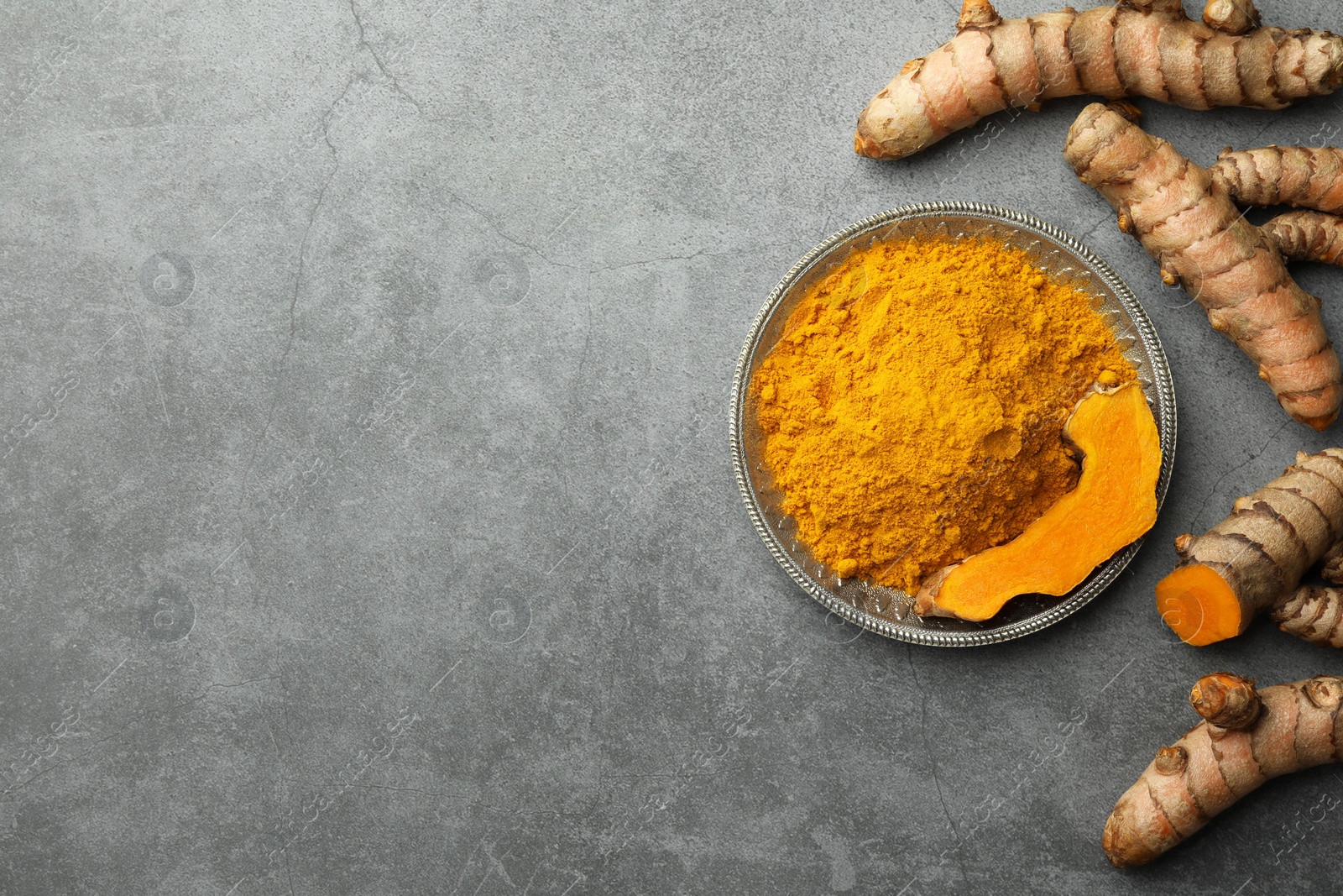 Photo of Plate with turmeric powder and raw roots on grey table, flat lay. Space for text