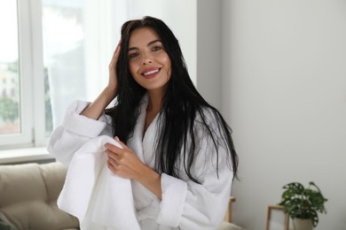 Photo of Beautiful young woman in bathrobe drying hair with towel indoors