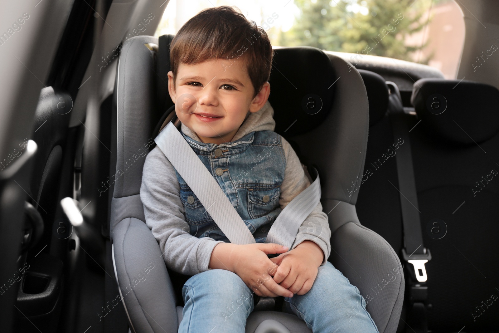 Photo of Cute little child sitting in safety seat inside car. Danger prevention