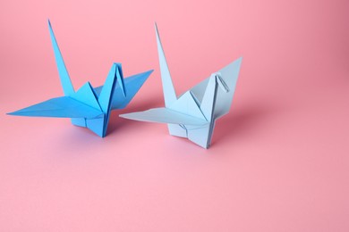 Photo of Origami art. Handmade paper cranes on pink background, space for text