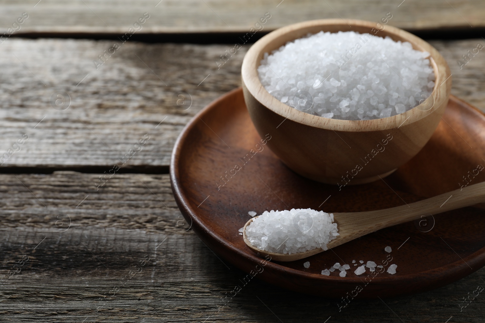 Photo of Organic salt in bowl and spoon on wooden table, closeup. Space for text