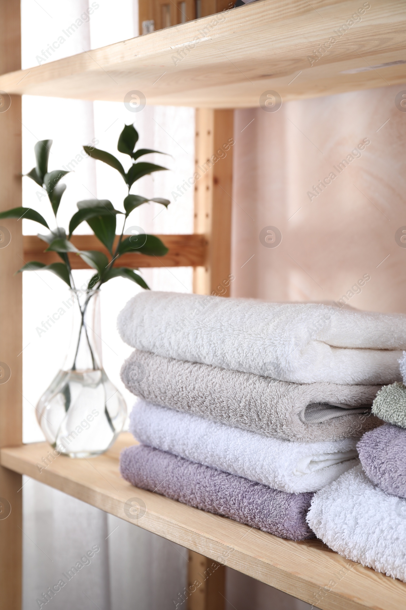 Photo of Stacked soft towels and green leaves on wooden shelf indoors