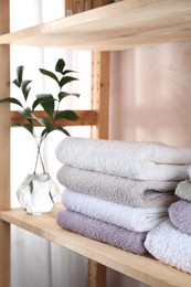 Photo of Stacked soft towels and green leaves on wooden shelf indoors