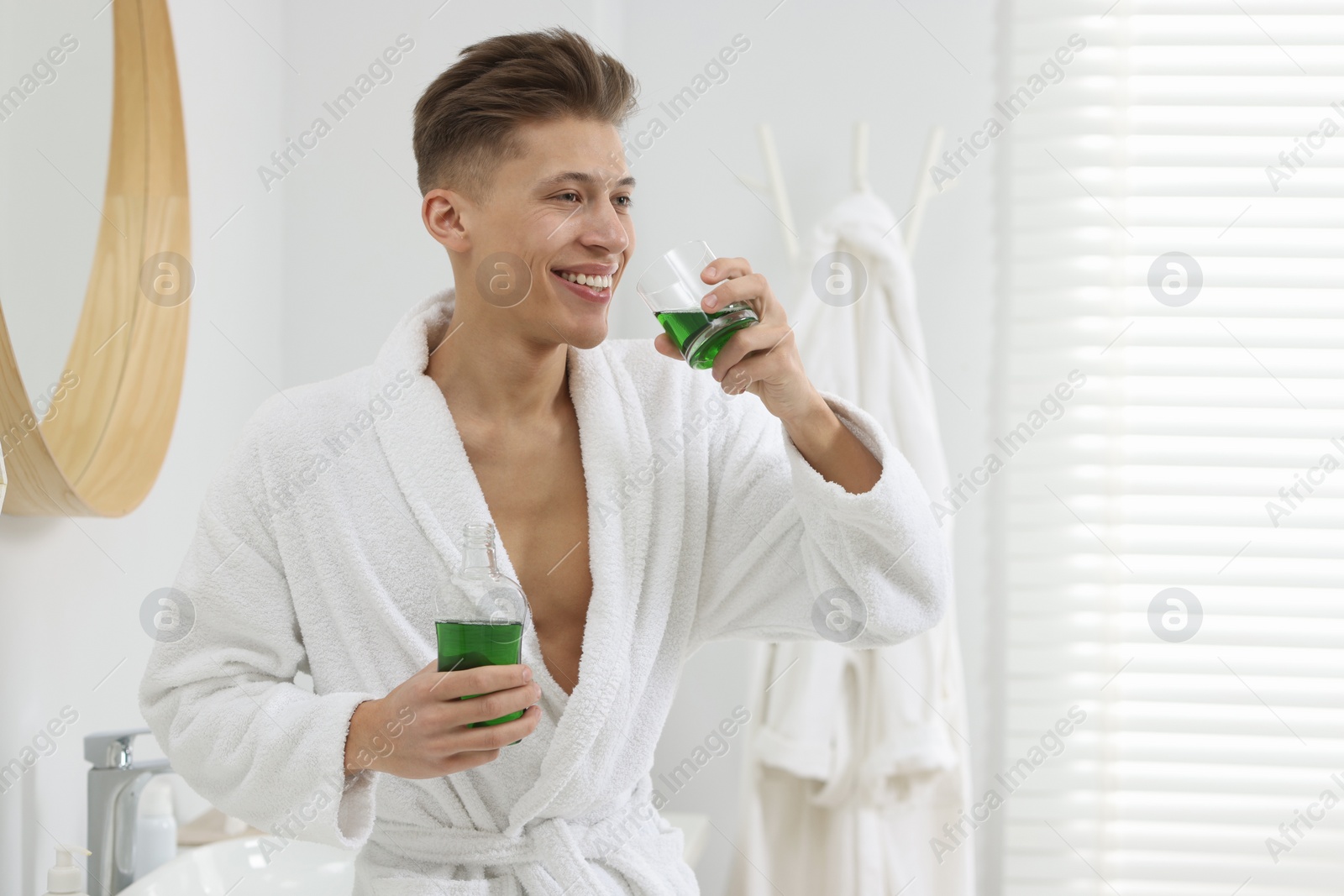 Photo of Young man using mouthwash in bathroom. Oral hygiene