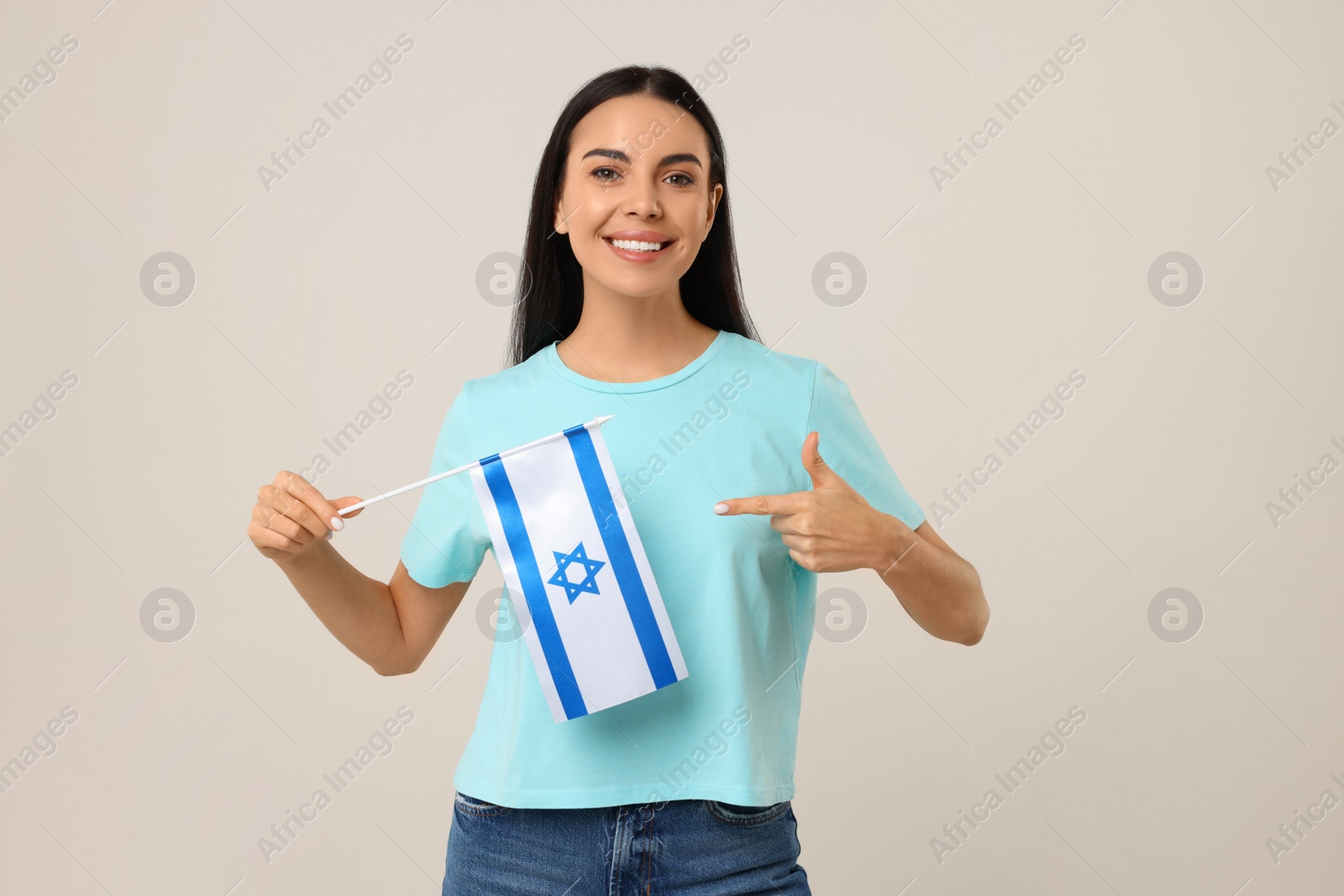 Photo of Happy young woman pointing at flag of Israel on beige background