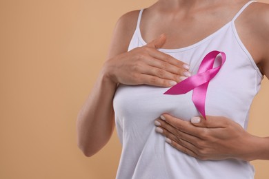 Photo of Breast cancer awareness. Woman with pink ribbon doing self-examination on light brown background, closeup. Space for text