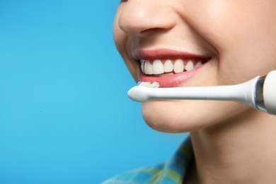 Photo of Young woman with electric toothbrush on color background, closeup. Space for text