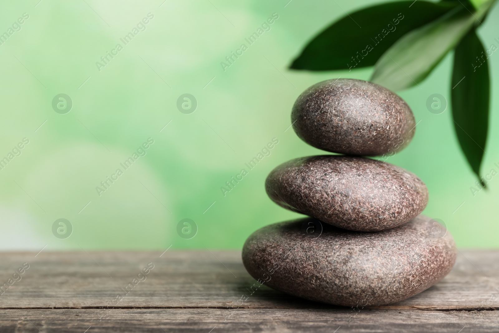 Photo of Stacked spa stones on wooden table against green bamboo leaves. Space for text