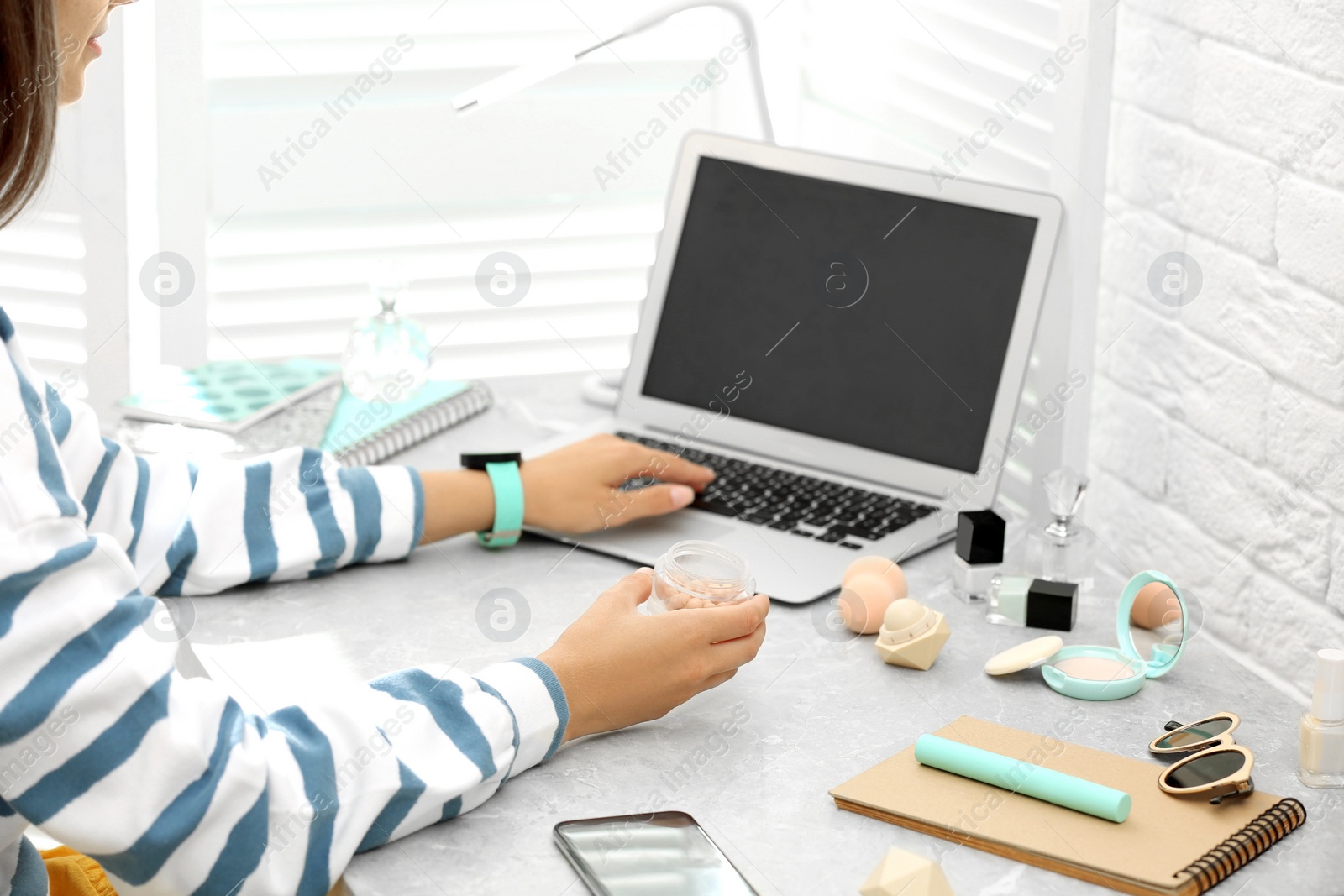 Photo of Young beauty blogger working on laptop at light grey marble table, closeup