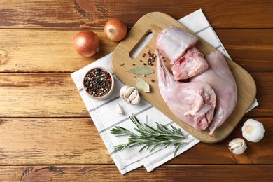 Photo of Fresh raw rabbit meat and spices on wooden table, flat lay. Space for text
