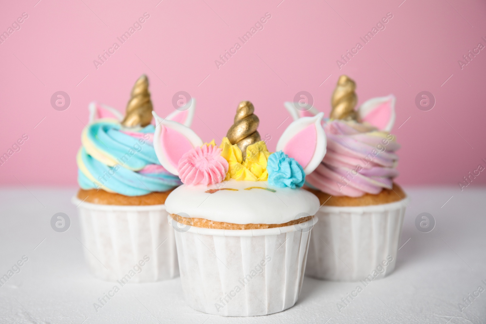 Photo of Three cute sweet unicorn cupcakes on white table