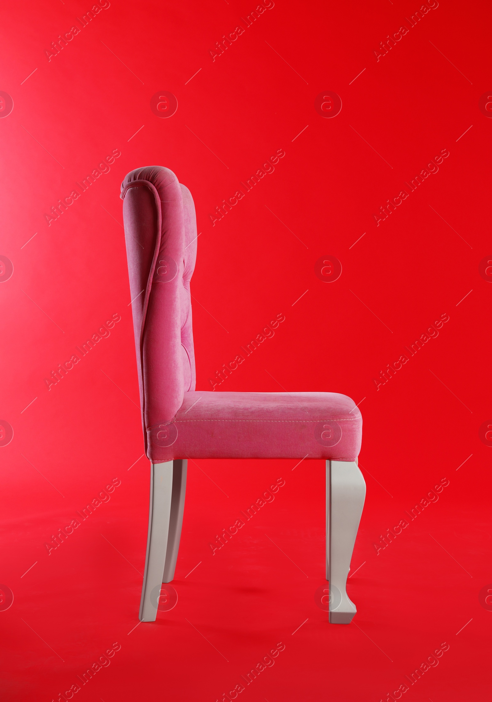 Photo of Stylish pink chair on red background. Element of interior design