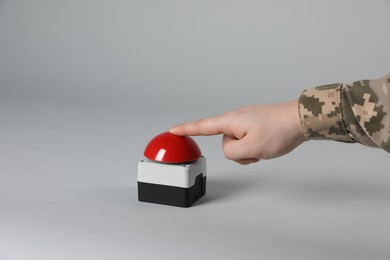 Serviceman pressing red button of nuclear weapon on light gray background, closeup. War concept