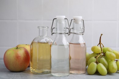 Photo of Different types of vinegar and fresh fruits on grey table