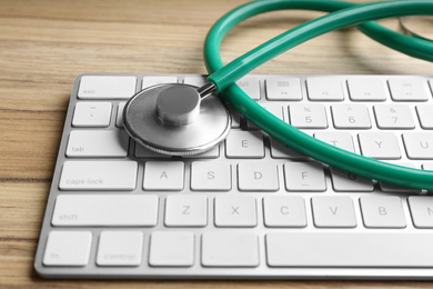 Photo of Keyboard and stethoscope on wooden table, closeup. Concept of technical support