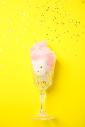 Glass with cotton candy on yellow background, top view