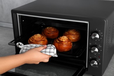 Woman taking out baking pan with delicious spiral buns from electric oven, closeup
