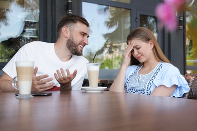 Photo of Young woman having boring date with talkative guy in outdoor cafe