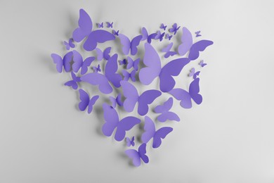 Image of Heart made of violet blue paper butterflies on white wall