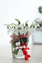Photo of Beautiful snowdrops with traditional martisor on table indoors. Symbol of first spring day