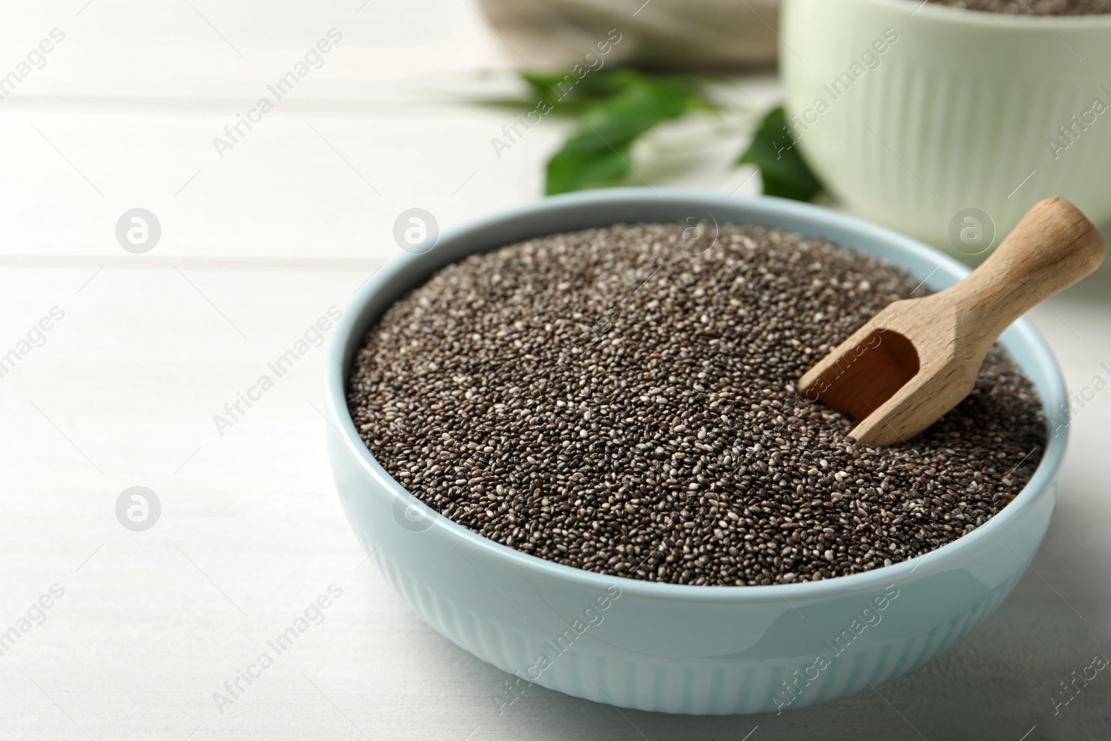 Photo of Bowl with chia seeds and wooden scoop on white table. Space for text