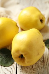 Photo of Fresh ripe organic quinces with leaves on white wooden table, closeup