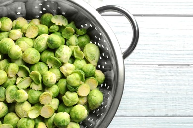 Photo of Colander with Brussels sprouts on wooden background, top view. Space for text