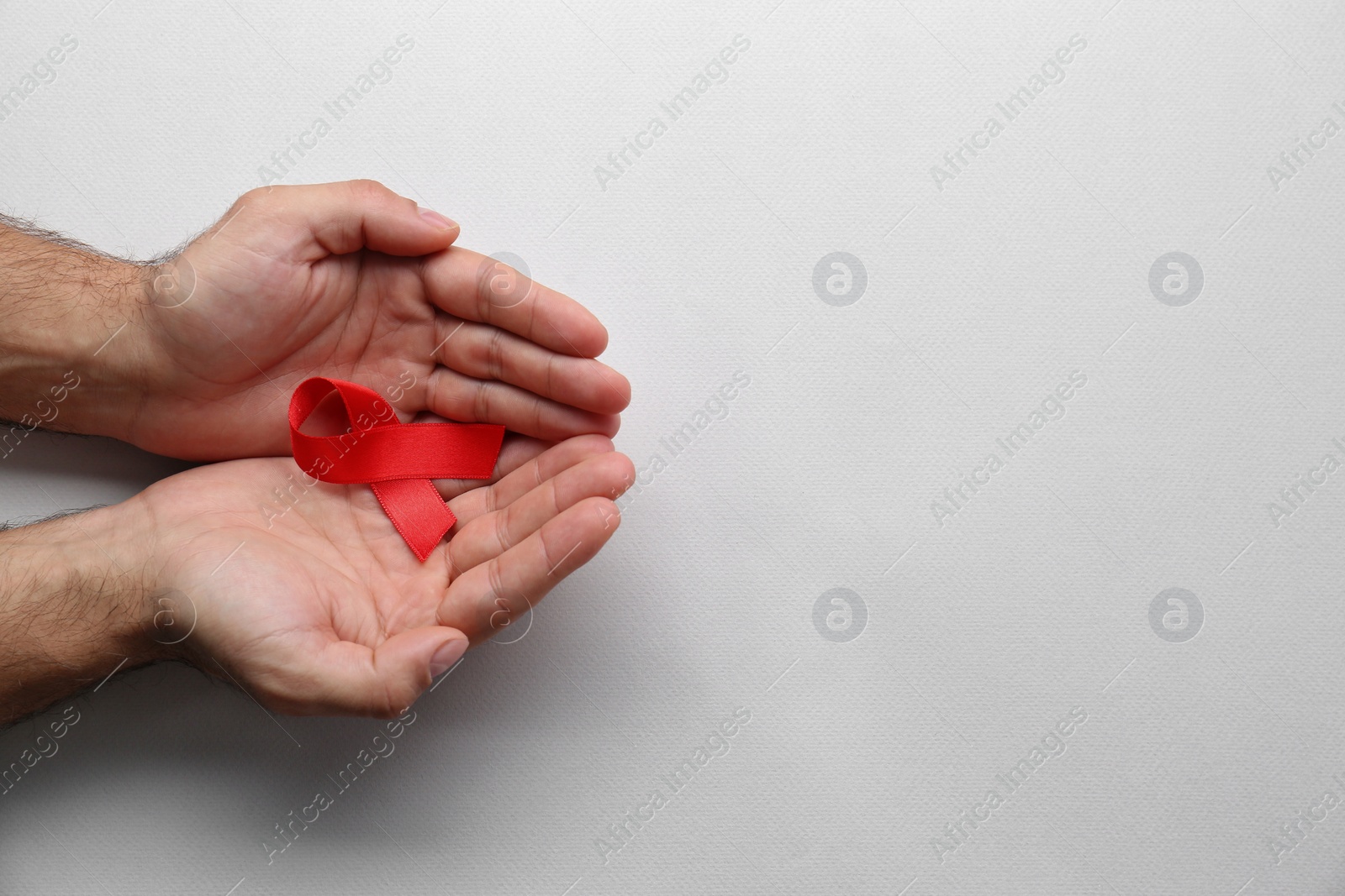 Photo of Man holding red awareness ribbon on white background, top view with space for text. World AIDS disease day