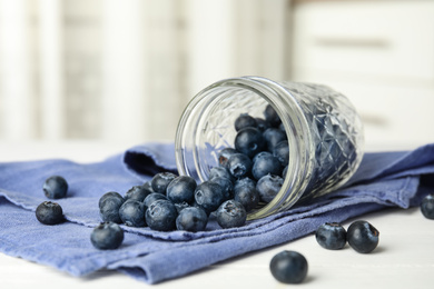 Photo of Overturned glass jar of ripe blueberries on white wooden table