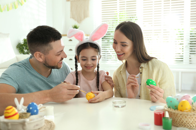 Photo of Happy father, mother and daughter painting Easter eggs at table indoors