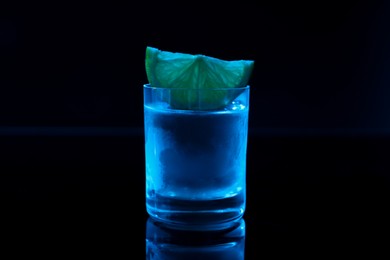 Photo of Shot glass of vodka with lime slice on dark background