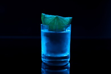 Shot glass of vodka with lime slice on dark background