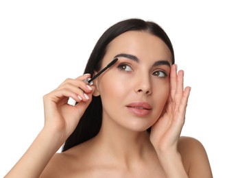 Beautiful young woman applying mascara on white background