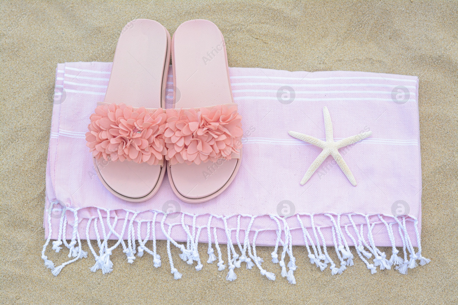 Photo of Blanket with stylish slippers and starfish on sand outdoors, top view. Beach accessories