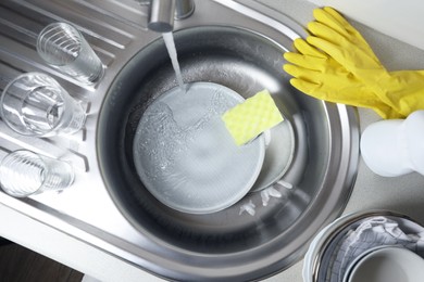 Photo of Washing plates, sponge and rubber gloves in kitchen sink, above view