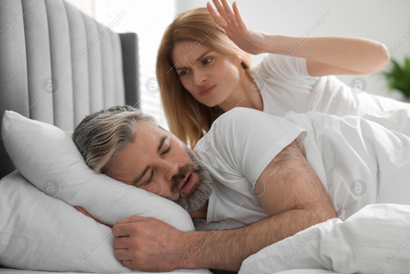 Photo of Irritated woman near her snoring husband in bed at home