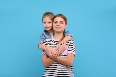 Photo of Little daughter hugging her mom on light blue background. Happy Mother's Day