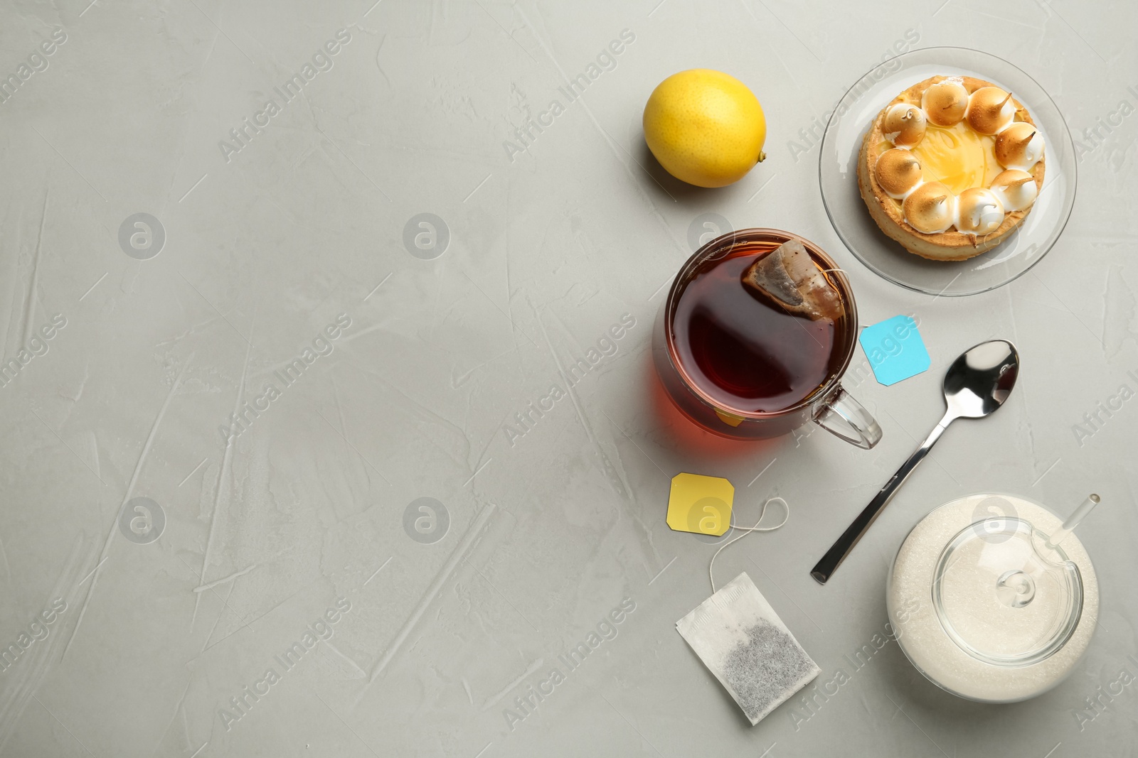 Photo of Flat lay composition with tea bag in ceramic cup of hot water and dessert on grey table. Space for text