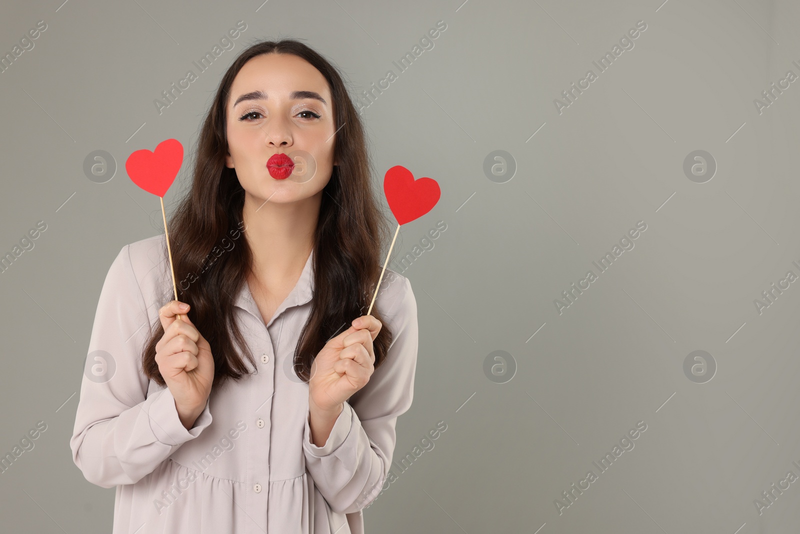 Photo of Beautiful young woman with paper hearts sending kiss on grey background, space for text