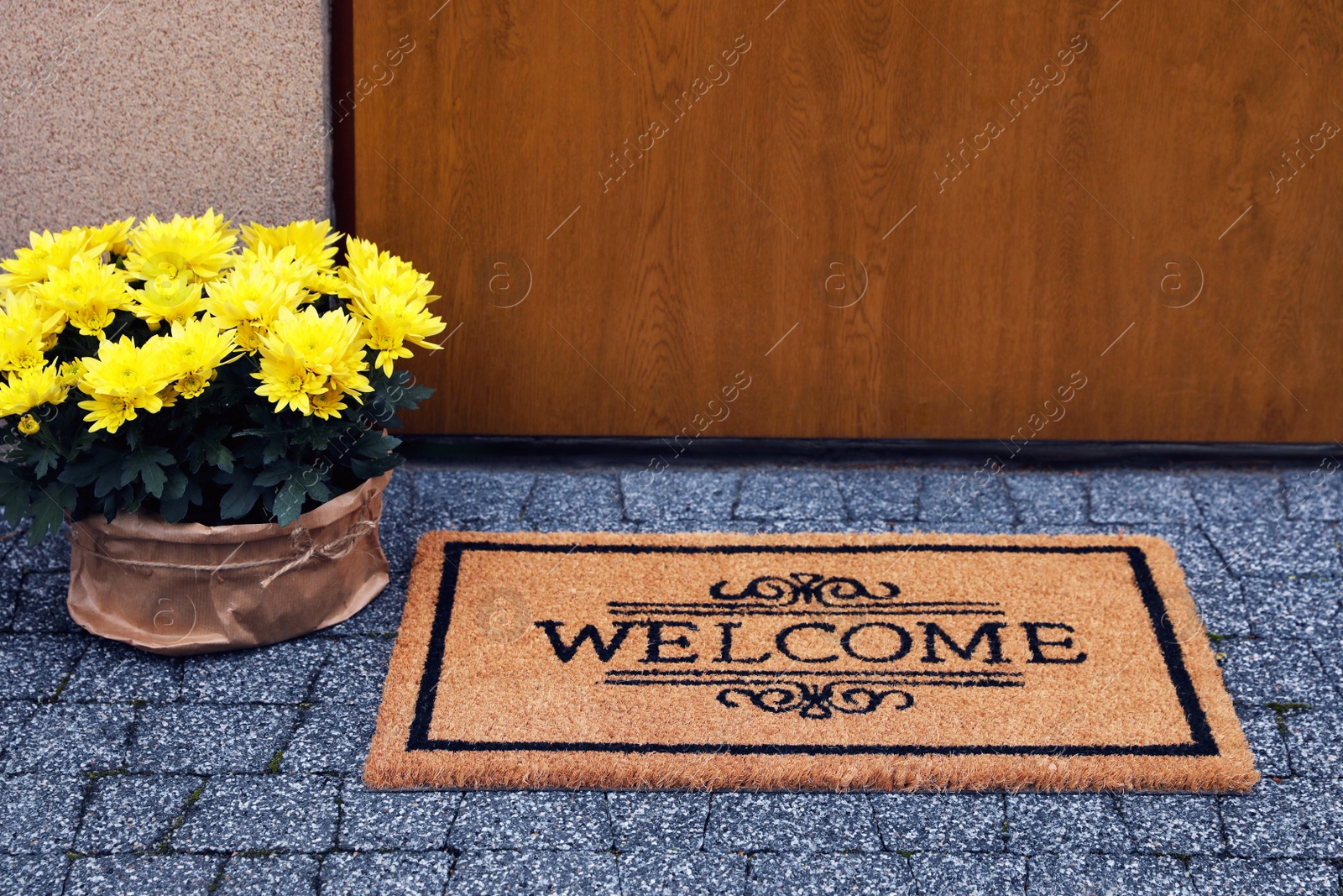 Photo of Doormat with word Welcome and beautiful flowers on floor near entrance