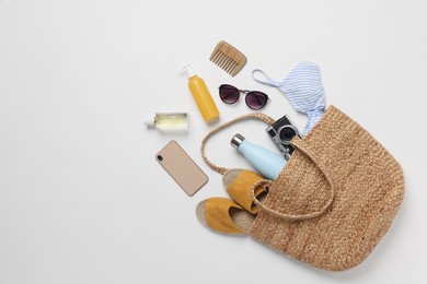 Wicker bag, smartphone and beach accessories on white background, flat lay. Space for text