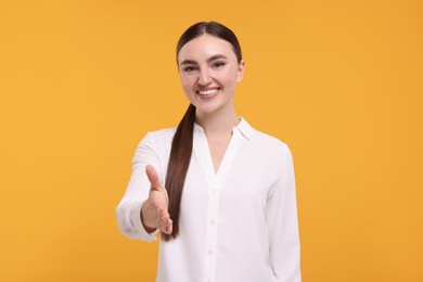 Smiling woman welcoming and offering handshake on orange background
