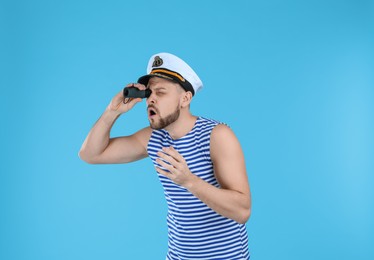 Photo of Sailor looking through monocular on light blue background
