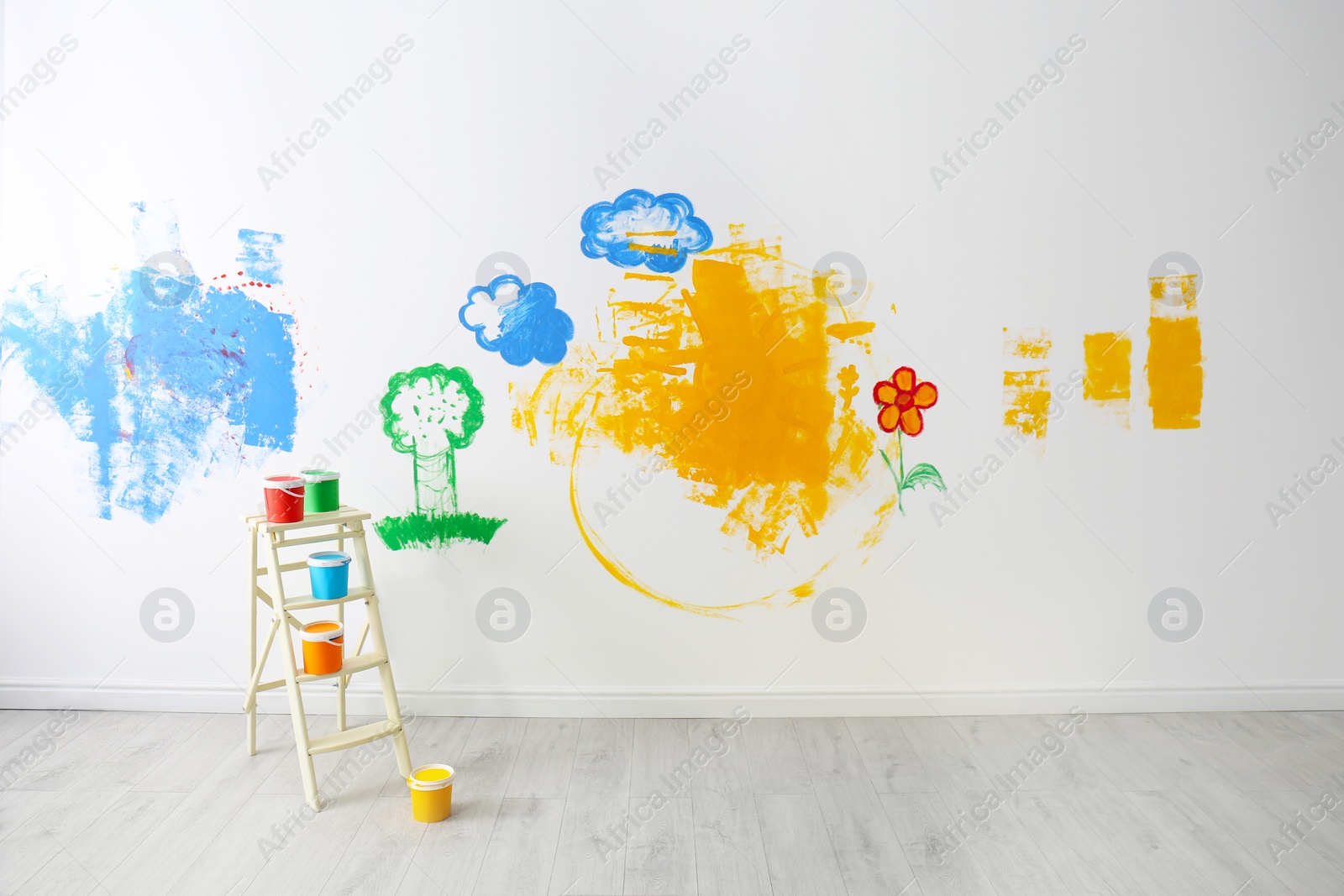 Photo of Ladder and colorful buckets near wall with children's paintings in room