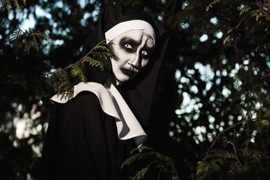 Photo of Portrait of scary devilish nun near tree outdoors. Halloween party look