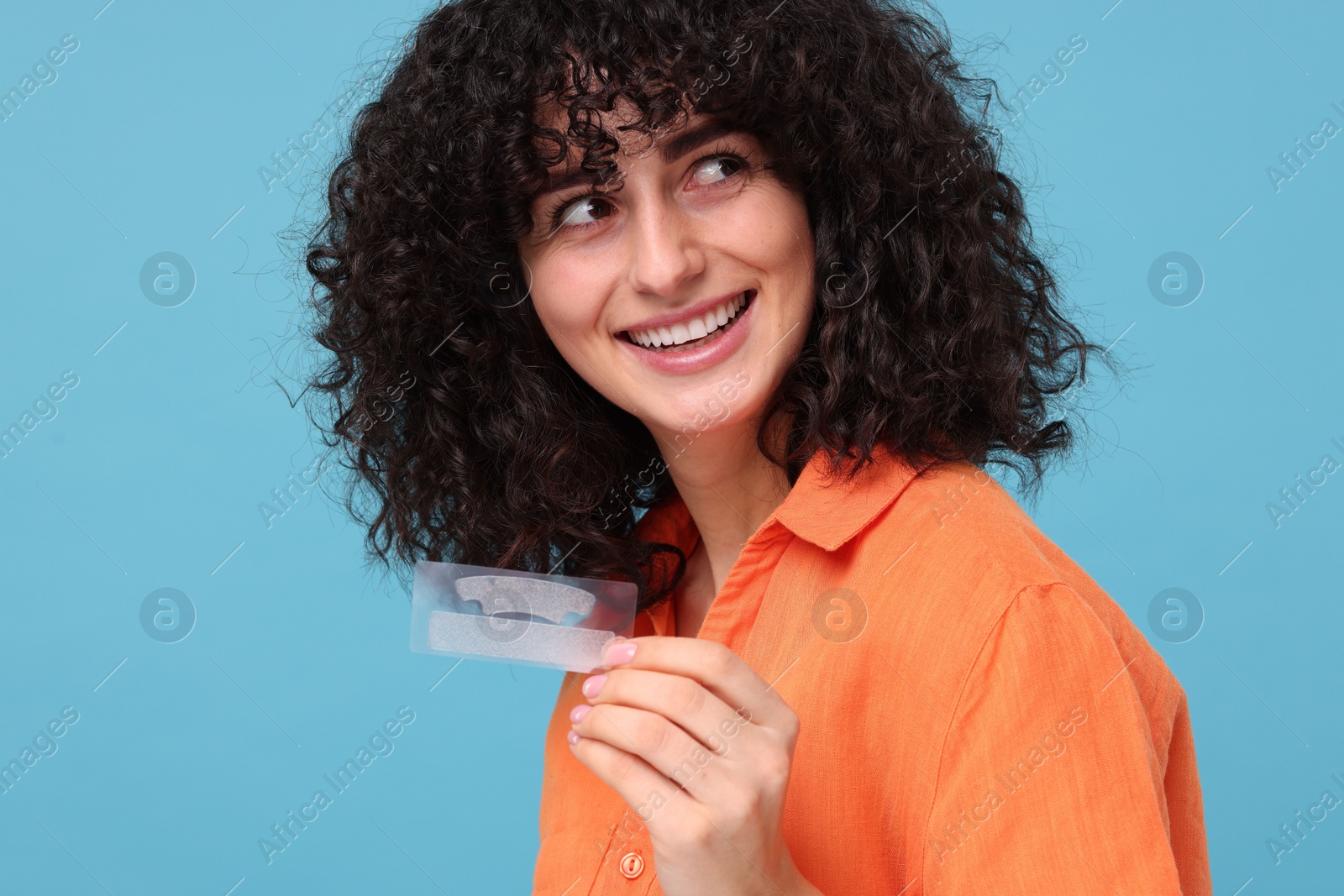 Photo of Young woman holding teeth whitening strips on light blue background